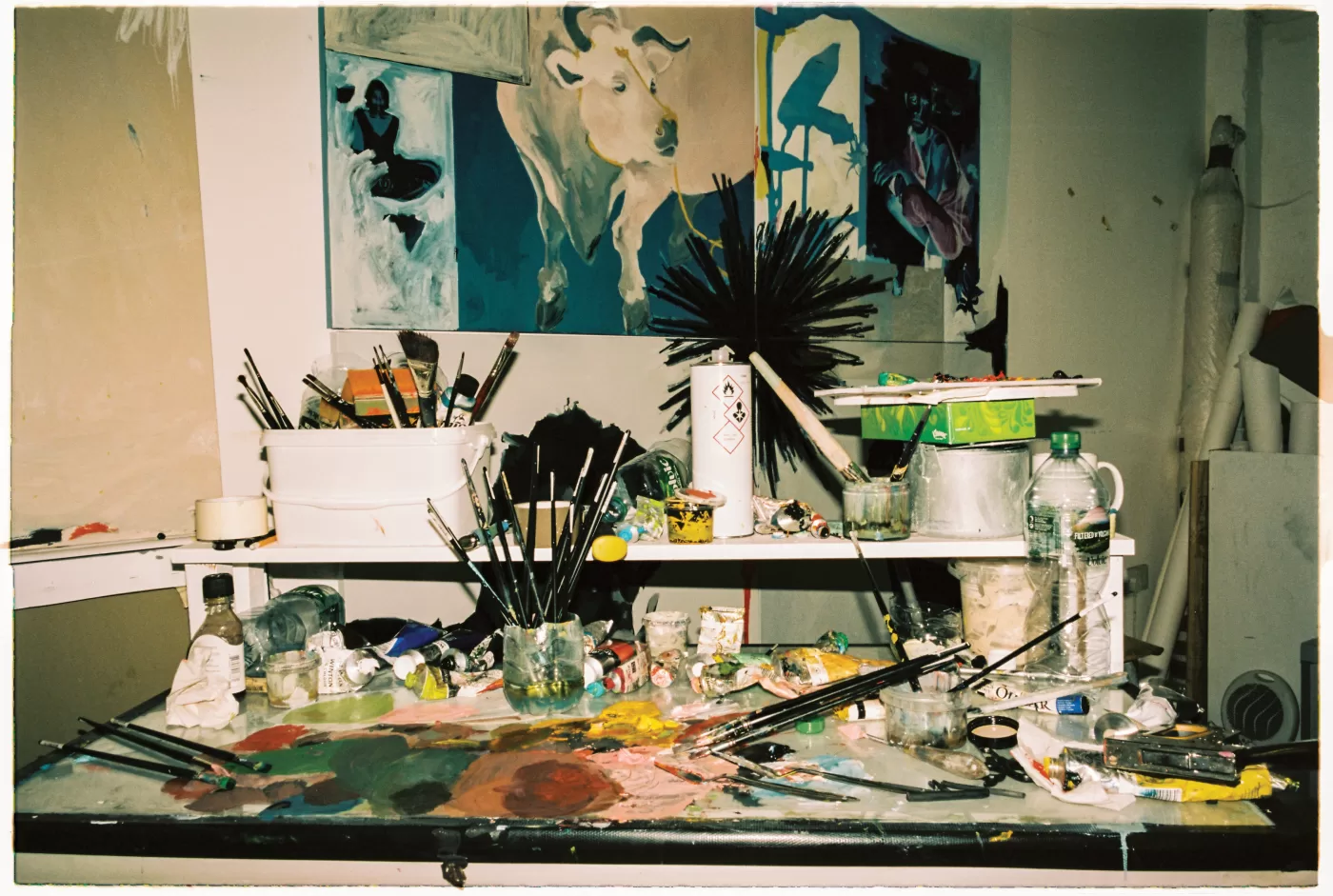 A photograph of the artist's workspace covered in painting materials