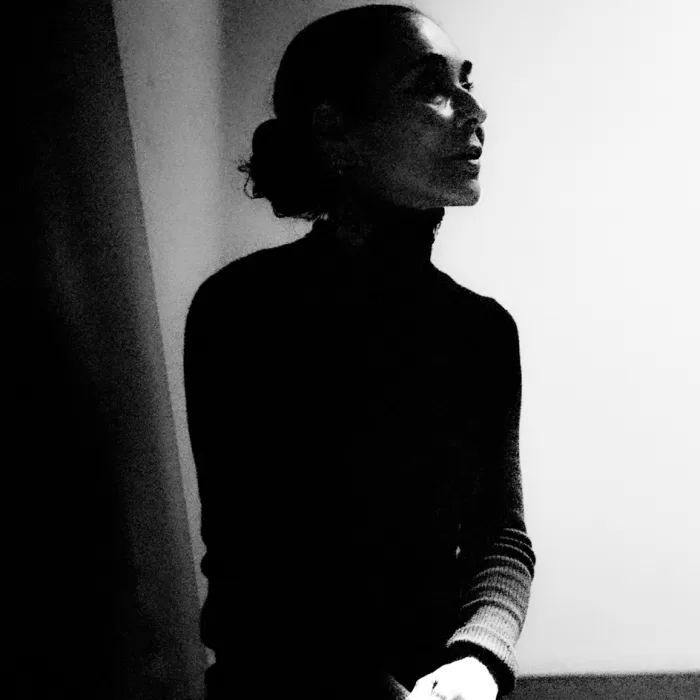 A black and white photograph of Shirin Neshat posing in her Brooklyn studio