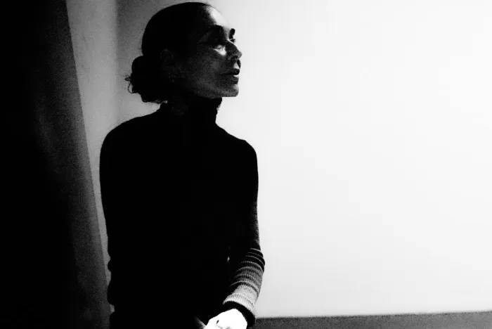 A black and white photograph of Shirin Neshat posing in her Brooklyn studio