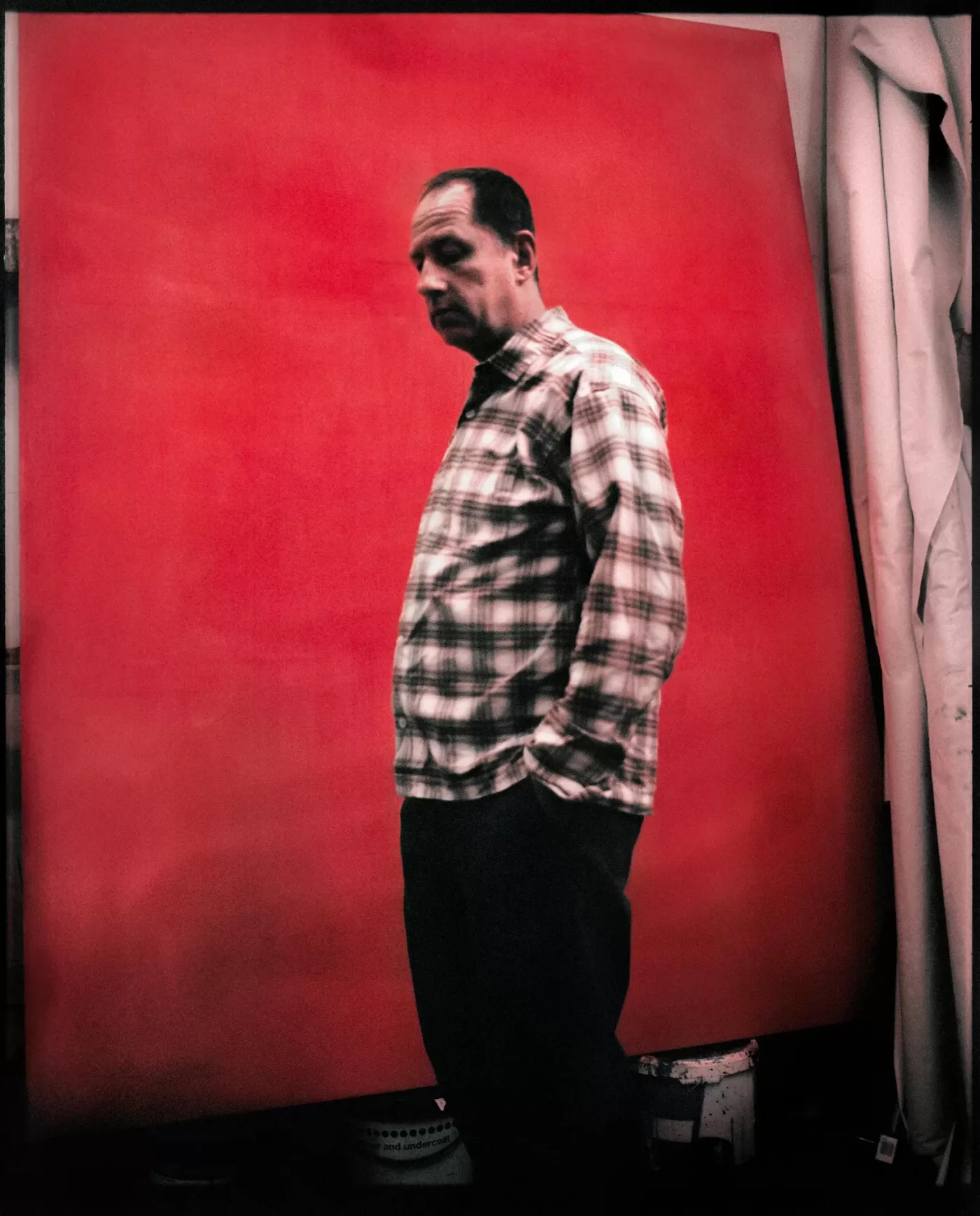 A photograph of Andrew Cranston stood with his hands in his pockets in front of a large red painted canvas