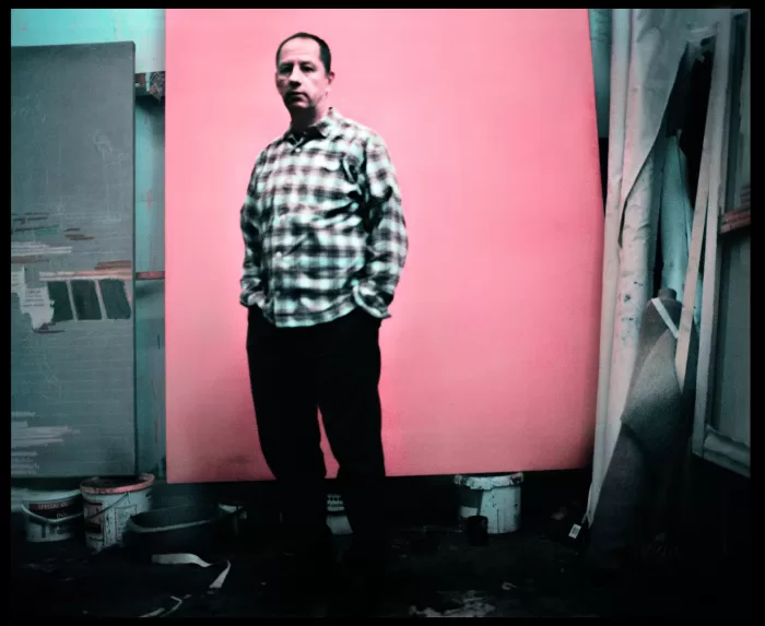 A photograph of Andrew Cranston stood in his studio in front of a large pink canvas