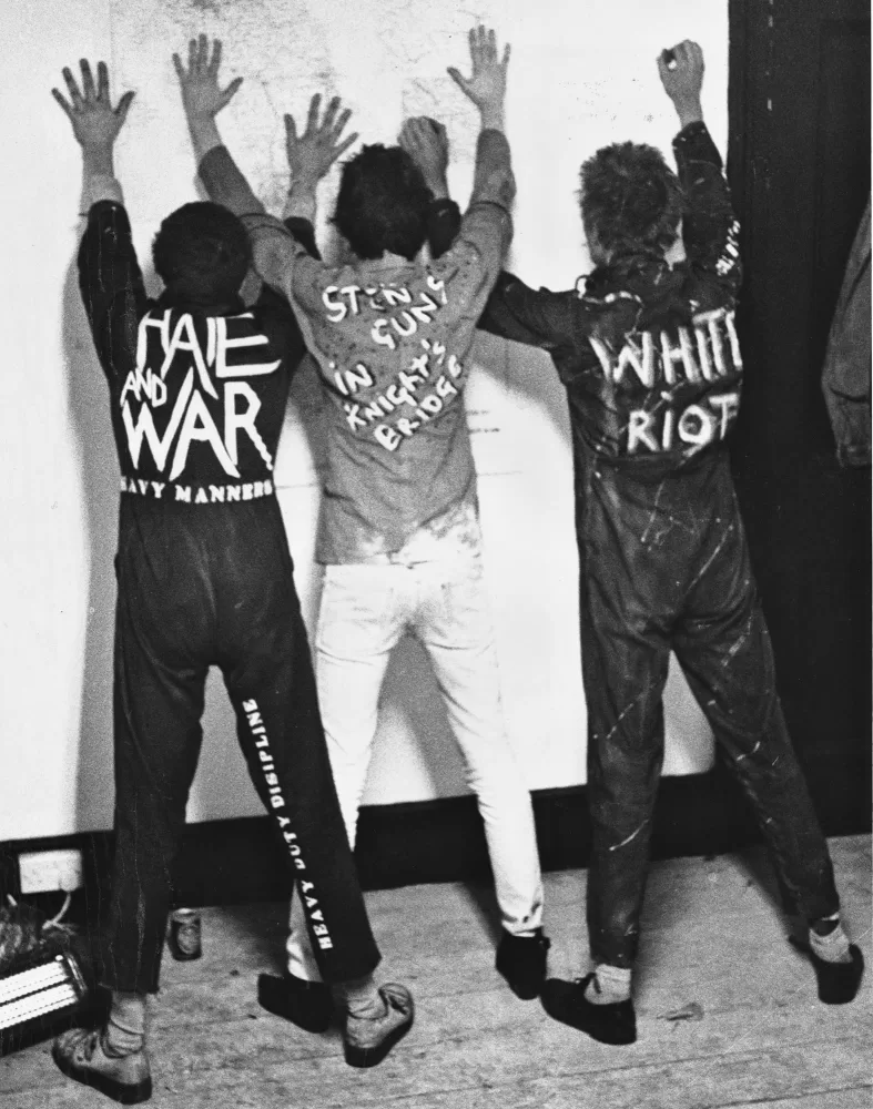 Black and white photograph of The Clash stood with their hands pinned up against a wall