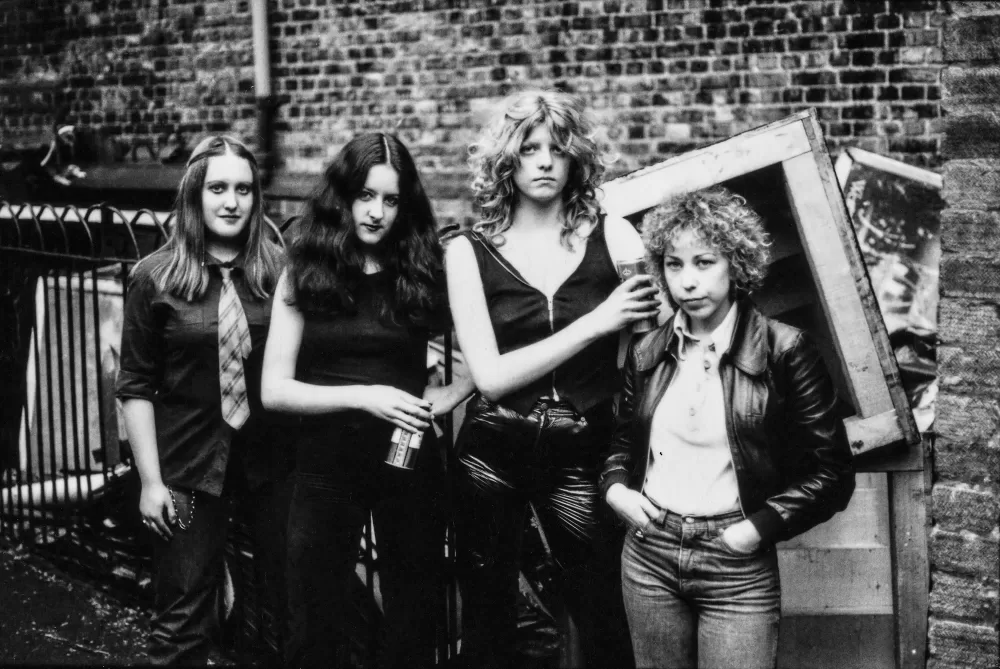 Black and white photograph of a group of four women stood in front of a brick wall