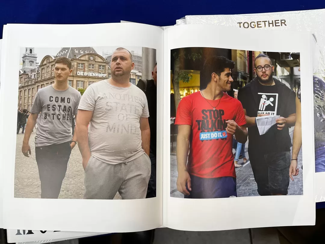 A photograph of a double-page spread from a photobook featuring candid photographs of people walking in the street wearing slogan t-shirts