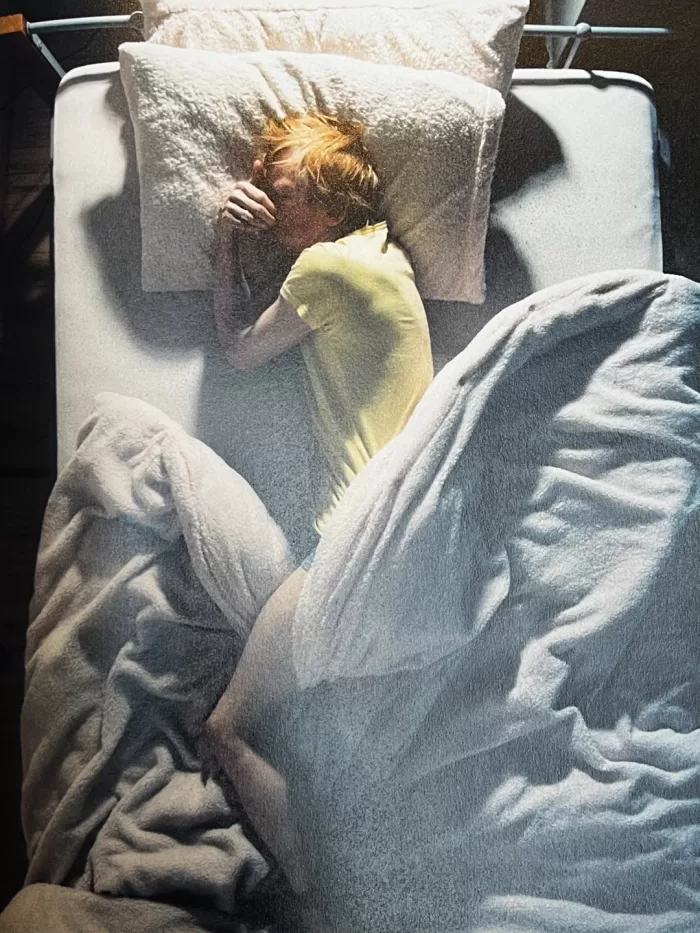 A photograph of a page from Dorothy Sing Zhang's book 'Like Someone Alive' picturing a person sleeping in bed