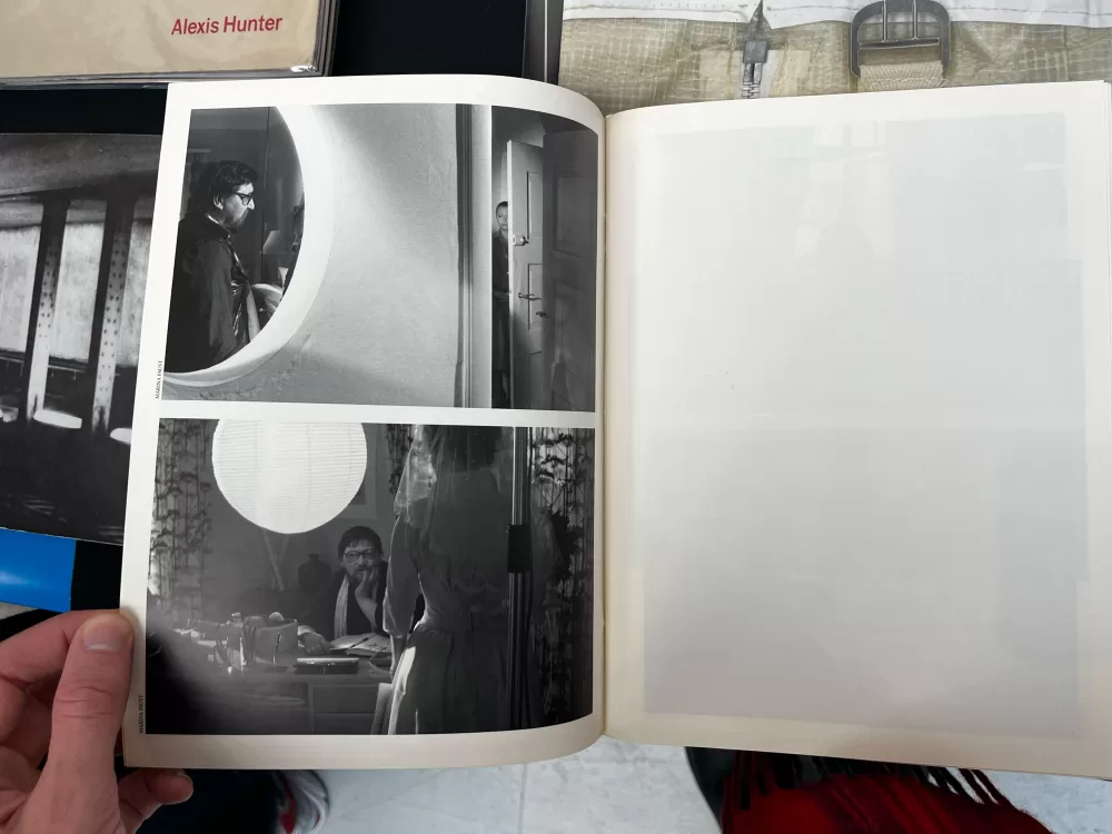 A photograph of a double-page spread from a photobook featuring two black and white photographs of people socialising in their home