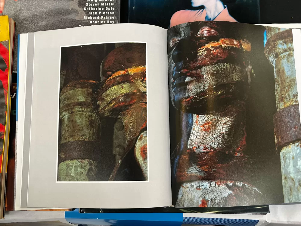 A photograph of a double-page spread from a photography book picturing a woman camouflaged with body paint