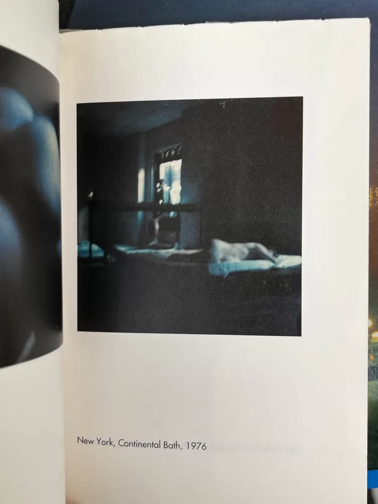 A photograph of a page from a photography book picturing someone lying naked in their bedroom