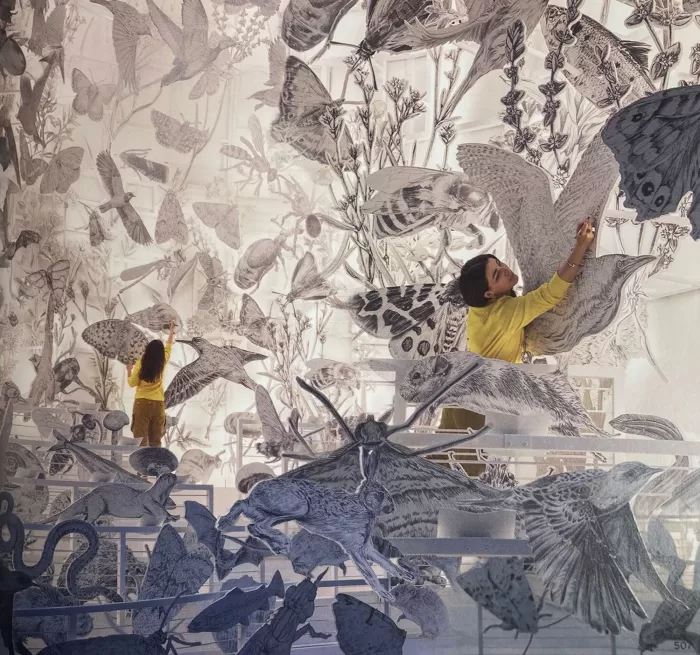 A photograph of Es Devlin in a room filled with large cut-outs of animals and insects