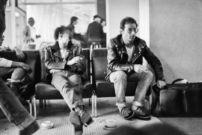 Black and white photograph of two men sat smoking in an airport