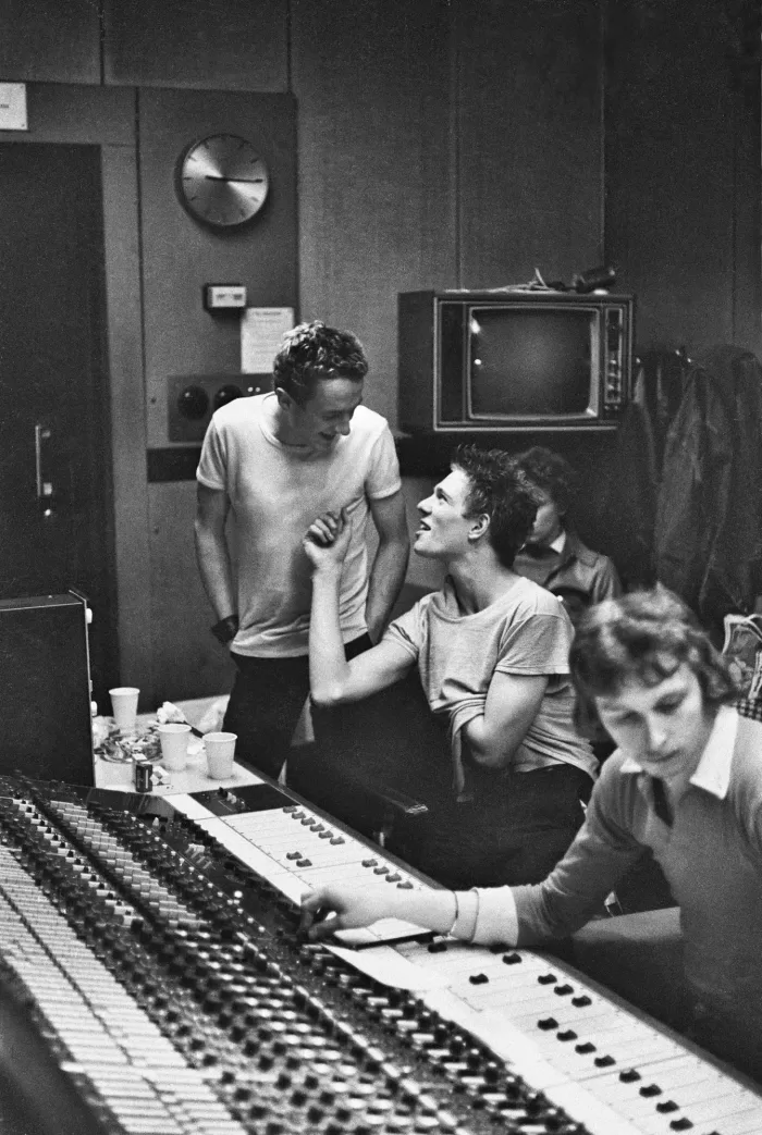 Black and white photograph of a band sat in a recording studio