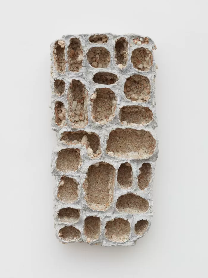 A photograph of a tiled oblong ceramic sculpture with a series of holes dug into it