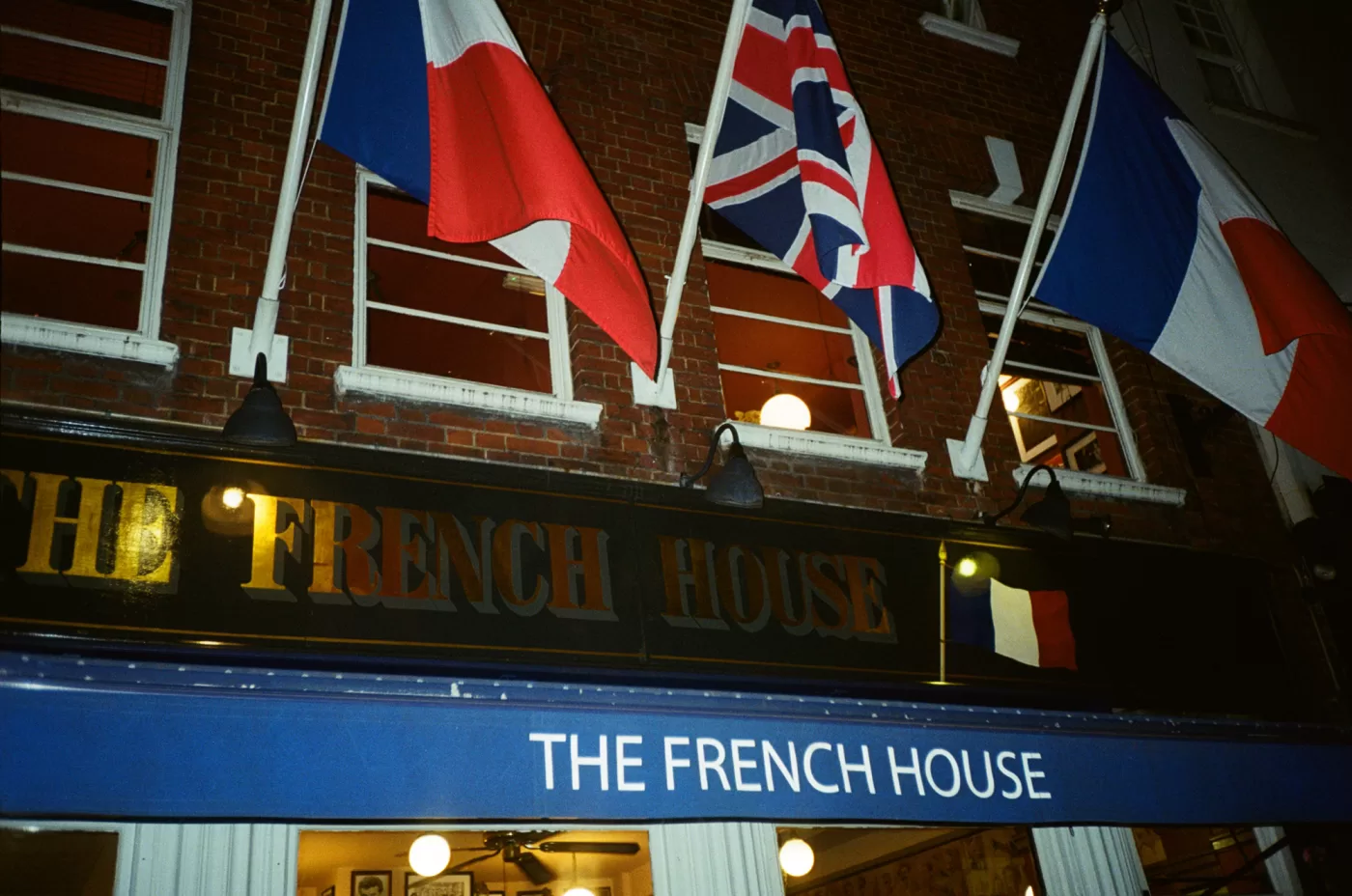 A flash photograph of the front of The French House, a pub in Soho, London. The front is adorned with British and French flags.