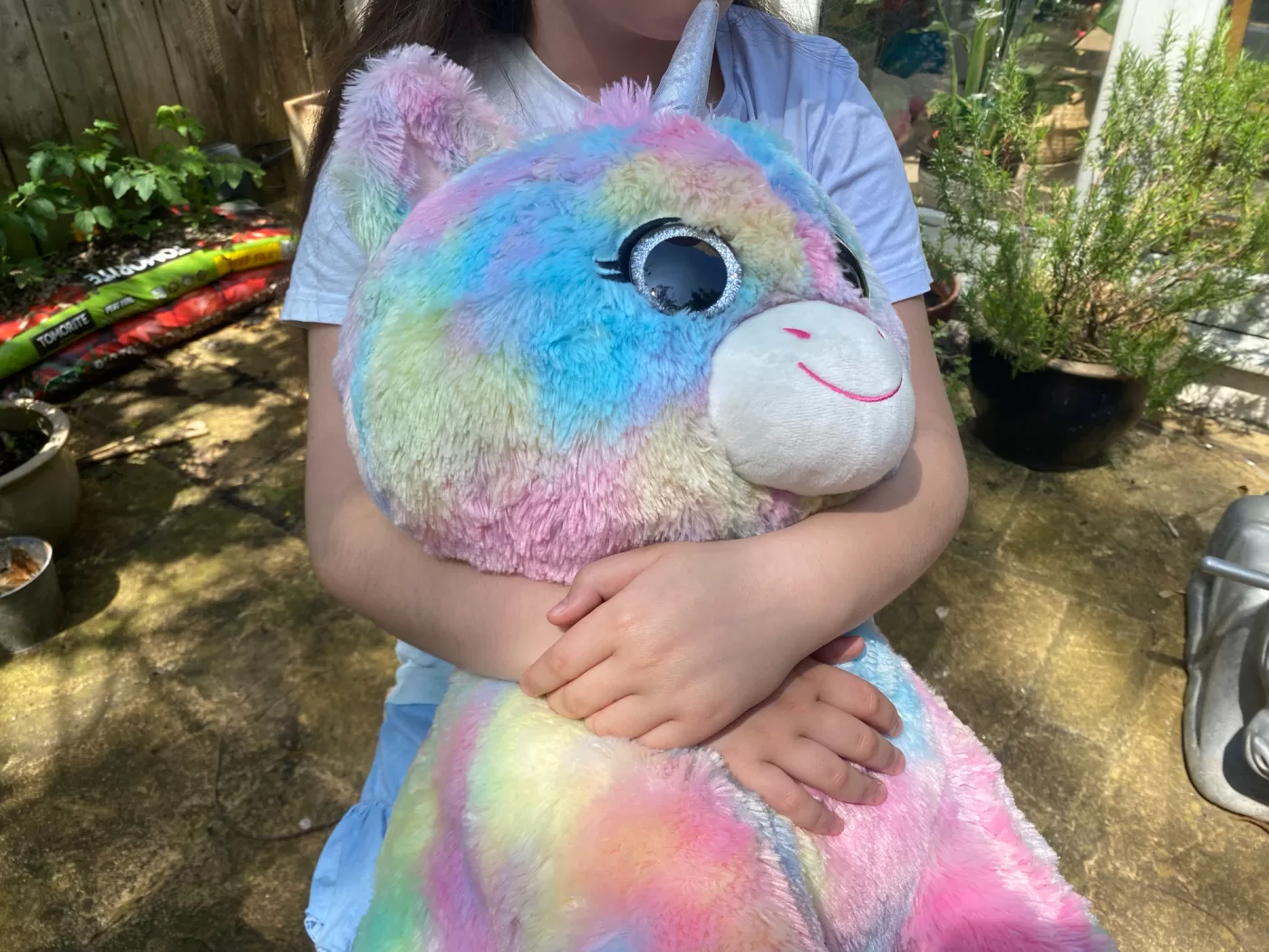 A photograph of Mark Leckey's daughter holding a rainbow unicorn toy. The toy features in his latest video DAZZLEDDARK