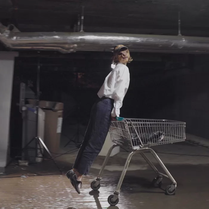 A photograph of a person wearing a pig mask and riding a shopping trolley.