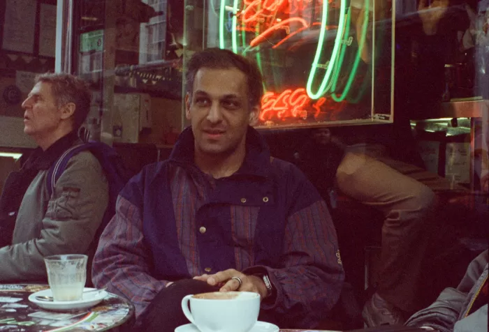 Abbas Zahedi photographed outside Bar Italia, with a neon sign lit up in the window behind him