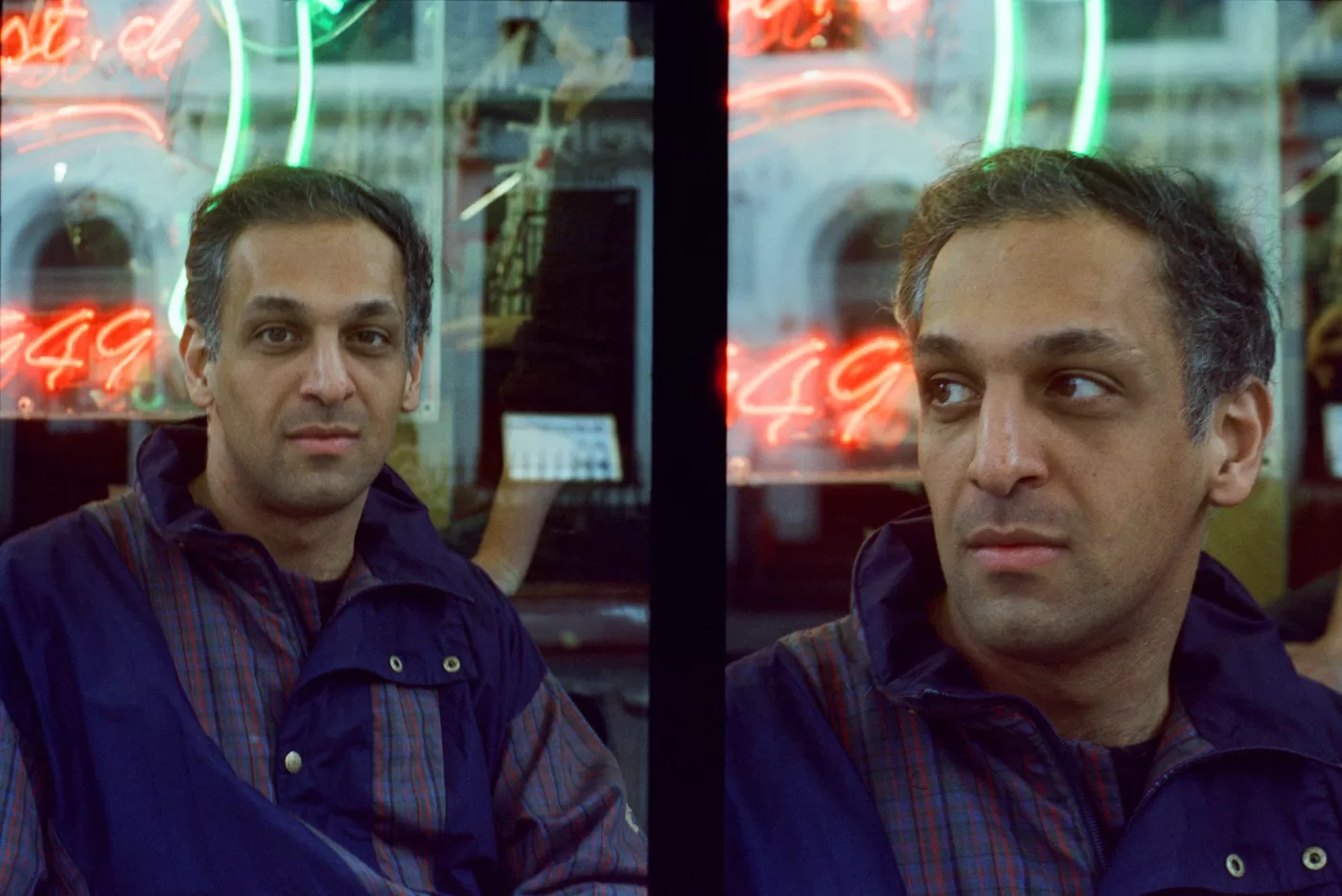 Abbas Zahedi photographed sitting at a table outside Bar Italia, with a neon sign lit up in the window behind him